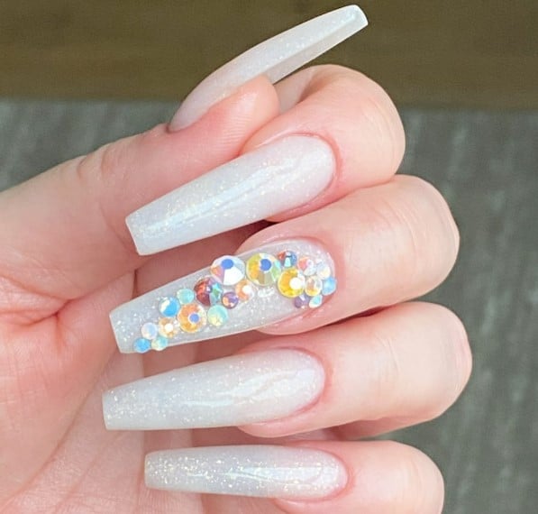 A person holding a white nail with crystals on it, showcasing exquisite coffin nails.
