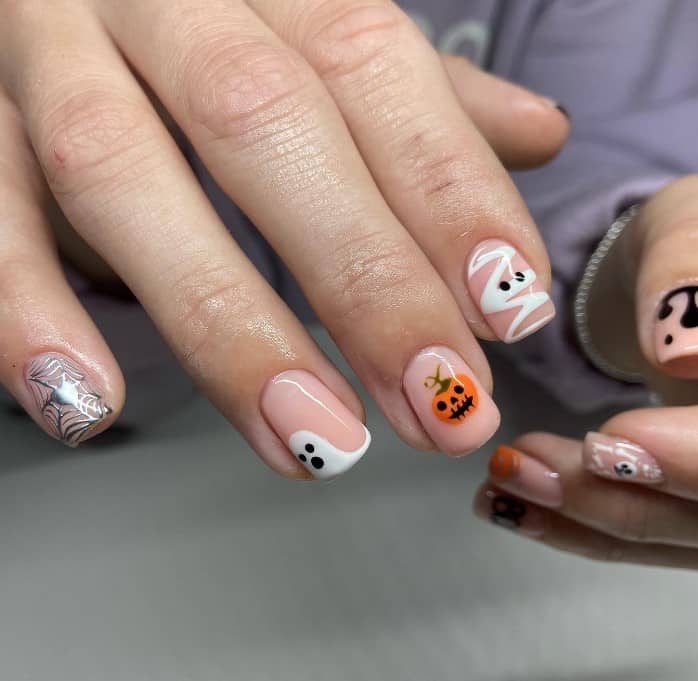 Short squares in creamy nude are rockin' a cute Halloween vibe with a mix of spooky styles: silver heart-centered spiderwebs, white ghost tips, orange skull pumpkins, a mummy ghost, and dripping black blood.
