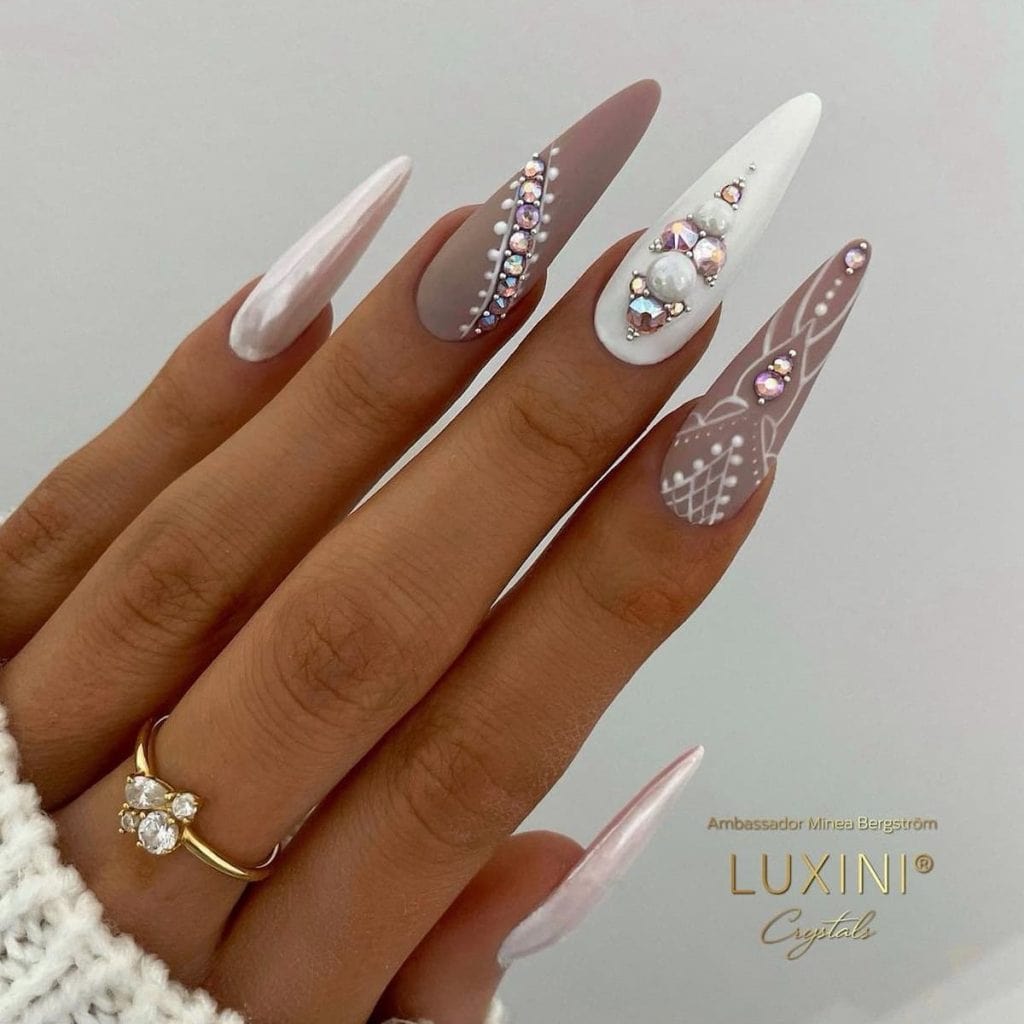 Taupe and white long almond nails alternate in matte and chrome finishes, adorned with pink rhinestones and intricate white nail art.