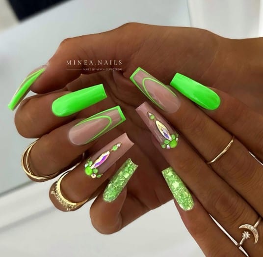 A woman confidently holding a glittery green coffin nail.