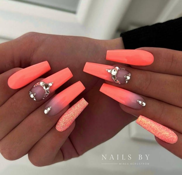 A pair of glossy coral coffin nails, with some nails topped with gold glitter