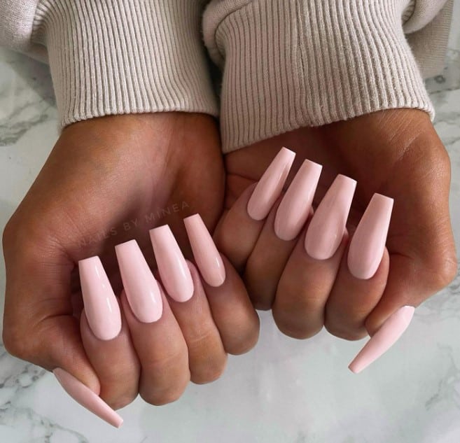 A woman's hands holding a pair of pink coffin acrylic nails.