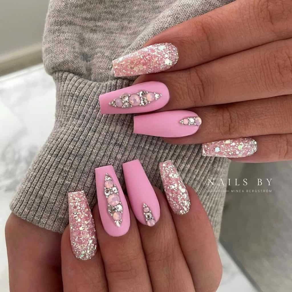 A woman's nails are adorned with a centerpiece of pink and crystal rhinestones, while others are dipped in sparkling silver and pink glitter