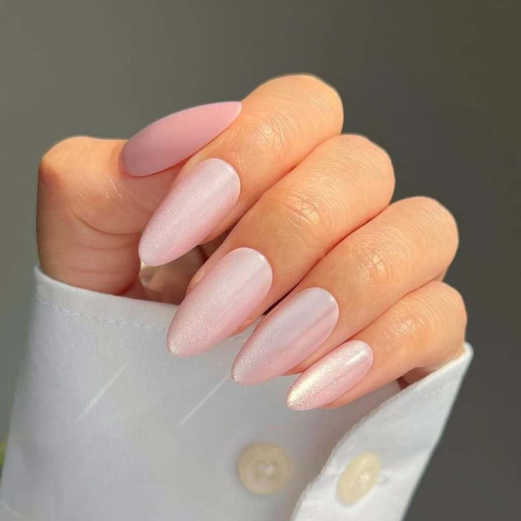 A woman's hand holding a pink chrome manicure, where light pink chrome powder graces each nail