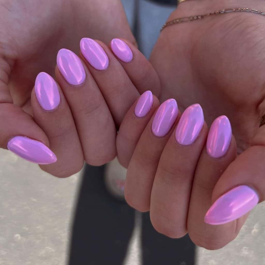 A woman's hands holding a pair of short pink chrome nails shine in a lustrous purplish hue