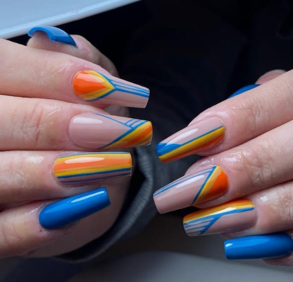 A woman's nails with whimsical geometric design on a nude base, artfully blending orange, yellow, and blue hues