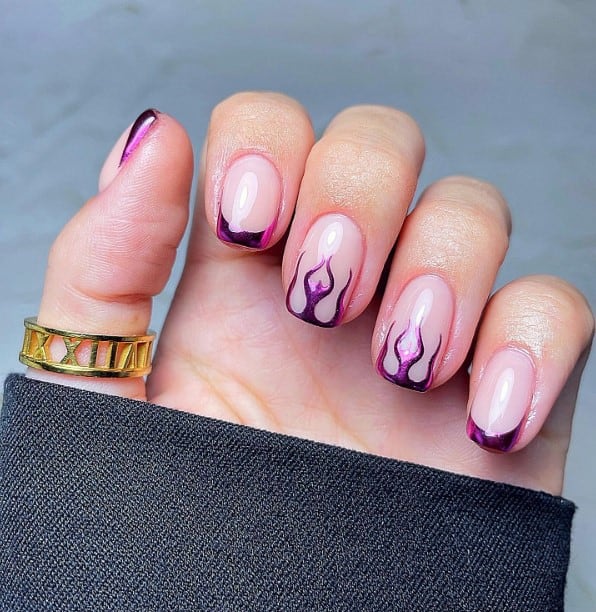 A woman's hand holding a light nude base on short squoval nails, three of which are crowned with metallic purple French tips