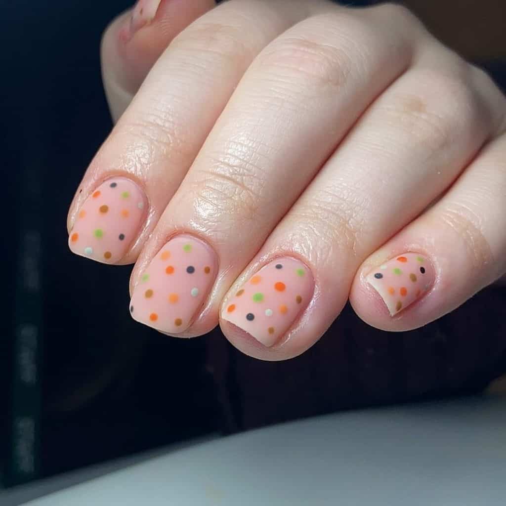 Short square nails come alive with the colors of fall as tiny dots in seasonal shades like ochre and navy blue embellish the matte pinkish nude base.