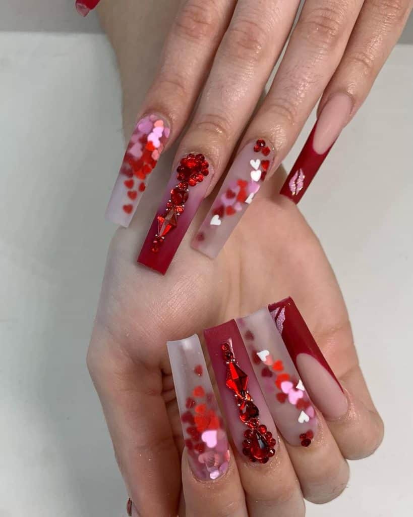 A woman's ombré nude and red matte nails with diamonds that come with pure nude ones adorned with dark red French tips and sparkling pink glitter kiss marks