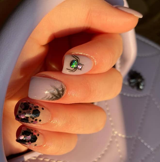 A woman's spiderweb nails feature short square nails in clear nude, adorned with a shower of black and metallic pink encapsulated chunky glitter.