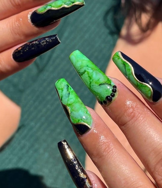 A woman's long coffin nails boast a glossy black canvas sprinkled with gold flakes