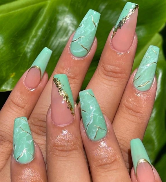 A woman's hand with mint green coffin nail design where two nail features a swirl of marble and shimmering gold chrome