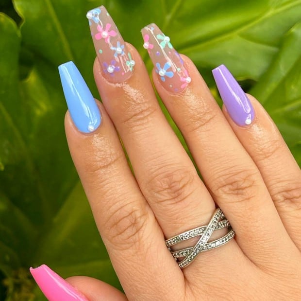 A woman's coffin nails is painted in a melody of pink, blue, and purple hues, each adorned with a small pearl near the cuticles.