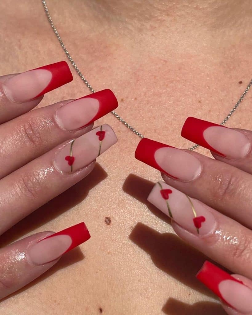 A woman matte cherry red nails that feature nude bases and striking red French tips