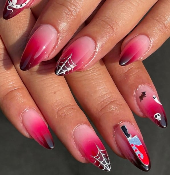 A woman's ombré almond nails fade from blood-red tips to rosy pink, topped with silver webs, a hissing snake, and a bloody knife