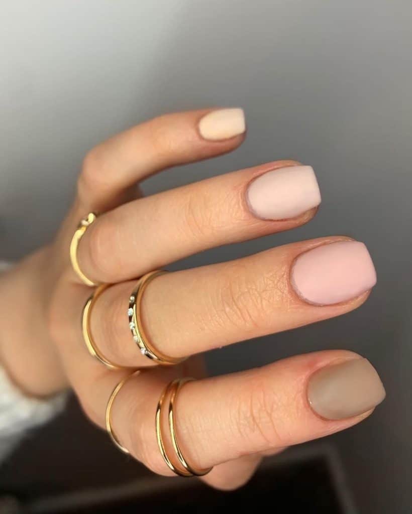 A set of squoval matte nude nails, each painted in a varying nude shade, seamlessly transitions from light to dark brown across the fingers for an elegant, modern look.
