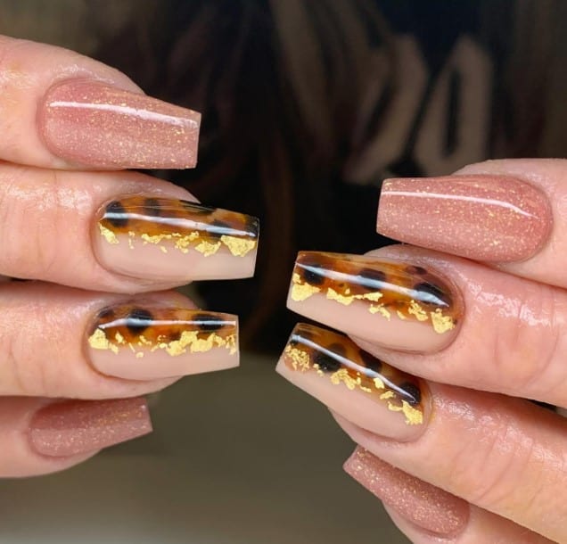 A woman's coffin-shaped nails featuring gold and leopard print designs.