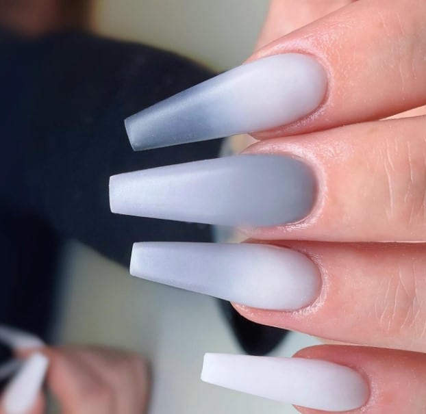 A woman is holding up a pair of grey and white ombre coffin nails.
