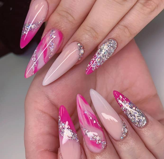 Pinkish nude nails in subtle ombré are a celebration, adorned with rhinestones near the cuticles and various designs in hot pink and silver glitter. 