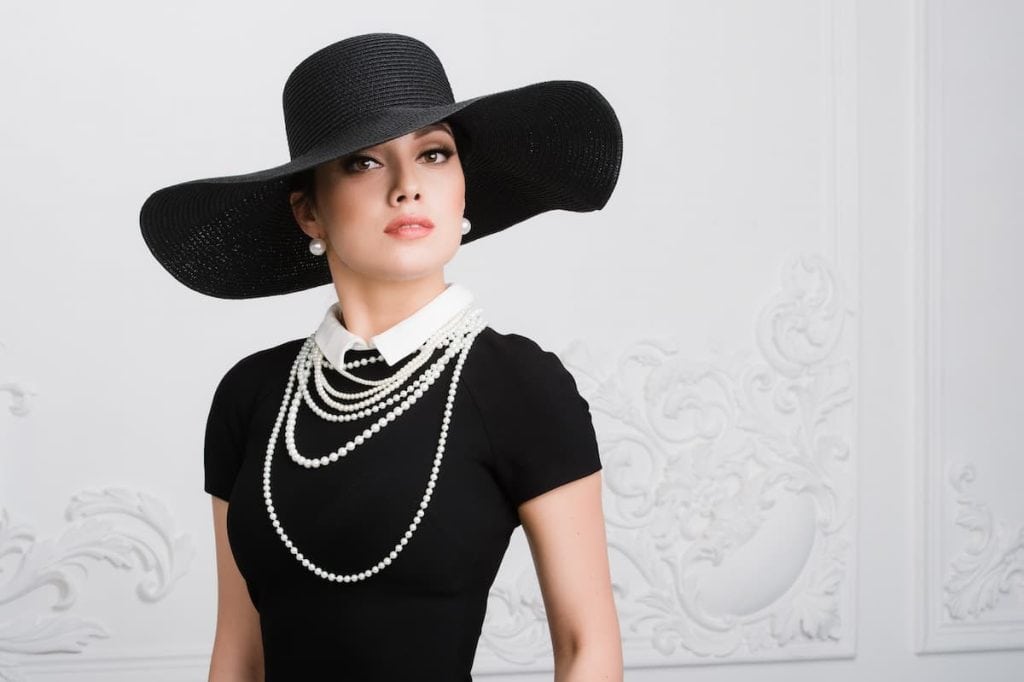A beautiful woman in a black hat and pearls layered necklace.