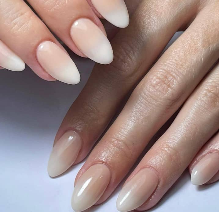 Ombré nude and white almond nails shine in a glossy finish, presenting a dreamy transition from natural to pure, like the first snowfall on a winter's day.