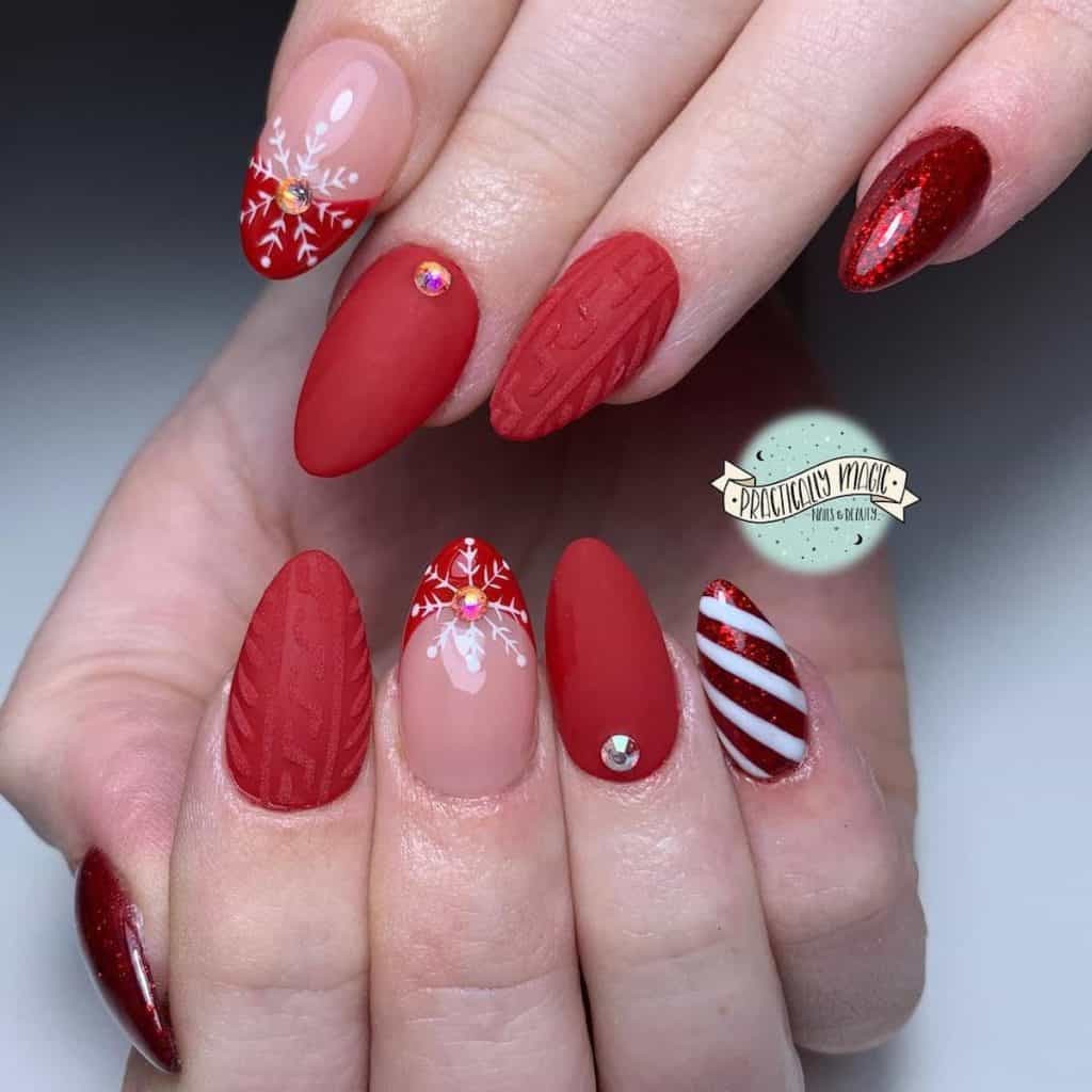 A woman's matte nails with a single rhinestone near the cuticles and glossy red French tips topped with white snowflake art and a central rhinestone
