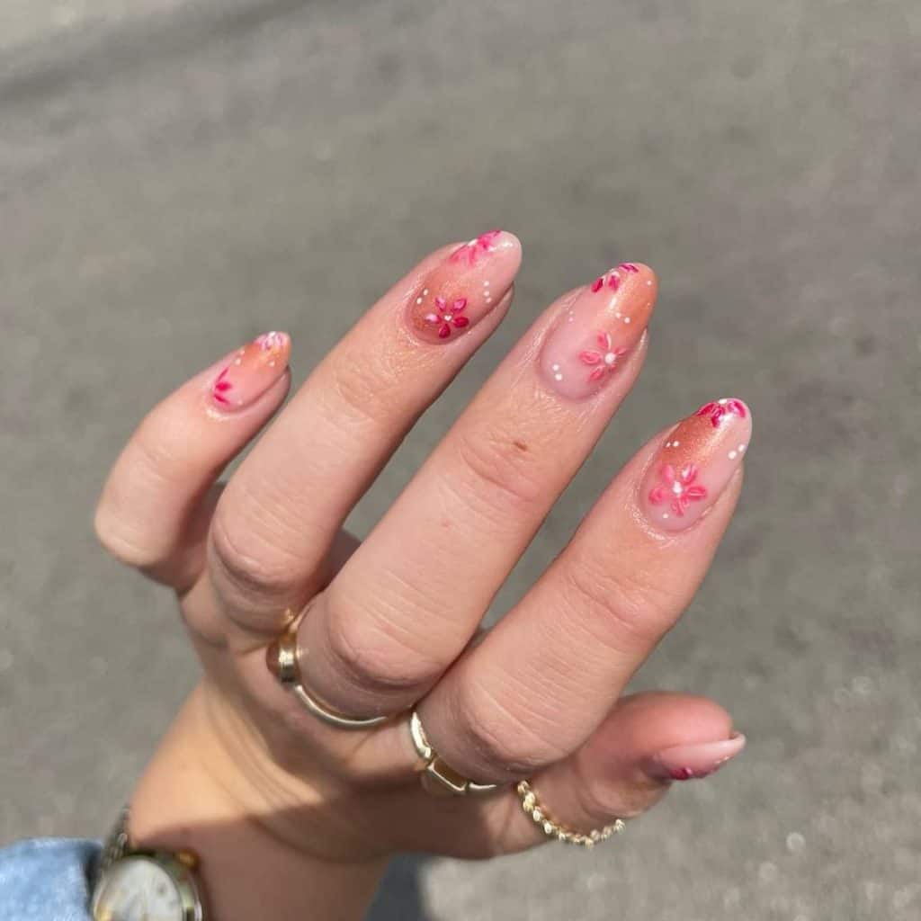 A woman's cute aesthetic nails as nude meets a gentle brush of copper, accented by nails with tiny white dots that mingle with blossoms of watercolor red petals