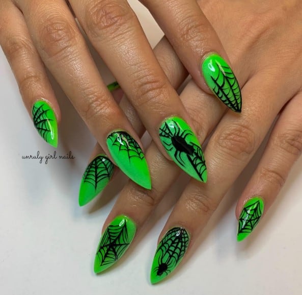 A woman with  long almond nails in neon green and black spider webs on her nails.