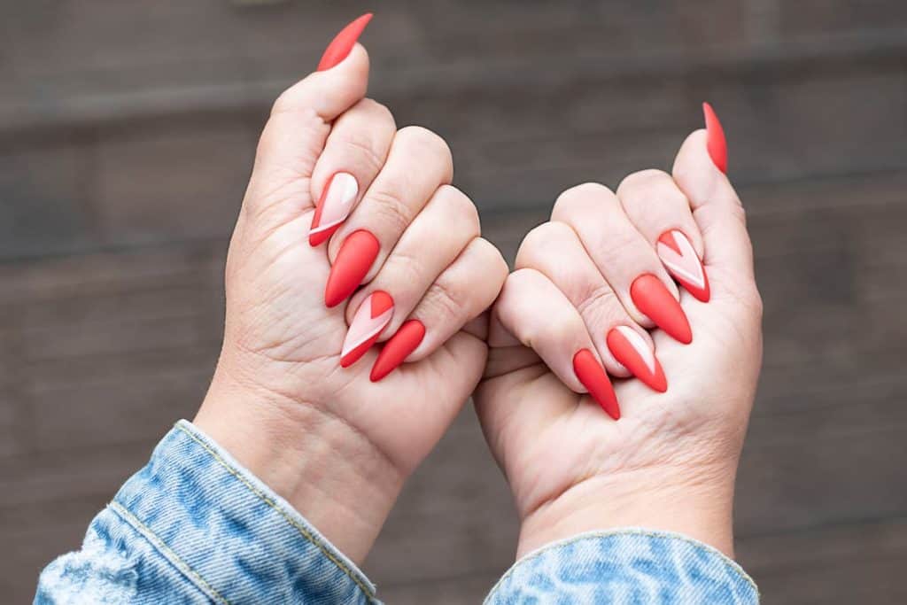 A woman's hands with red nails holding up a denim jacket.