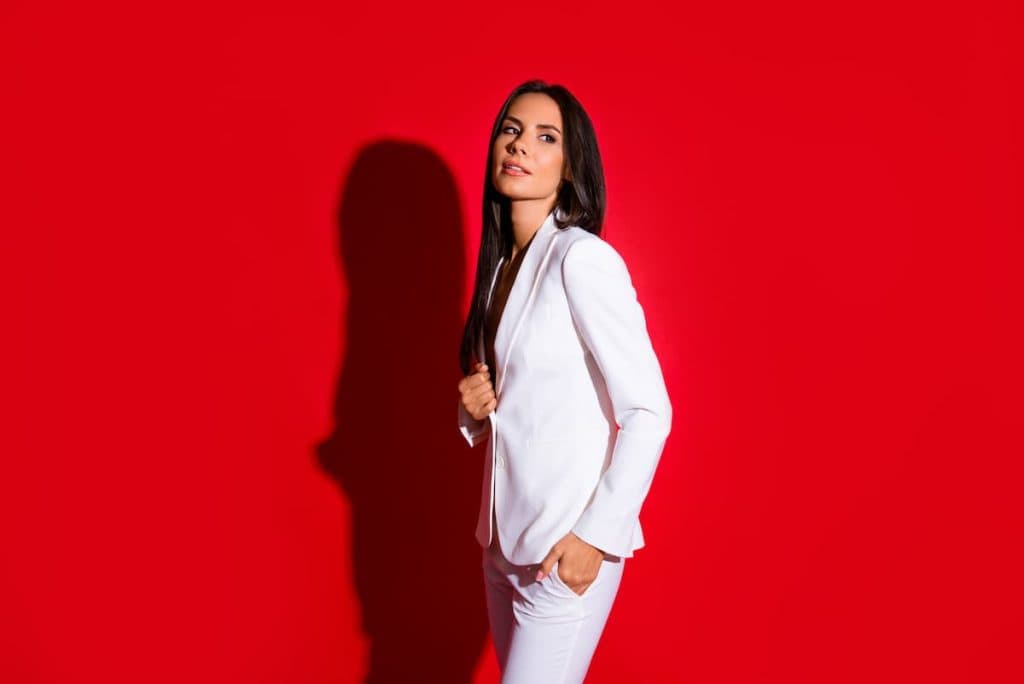 Side view portrait of gorgeous charming woman in white suit holding hand in pocket looking away isolated on bright red background
