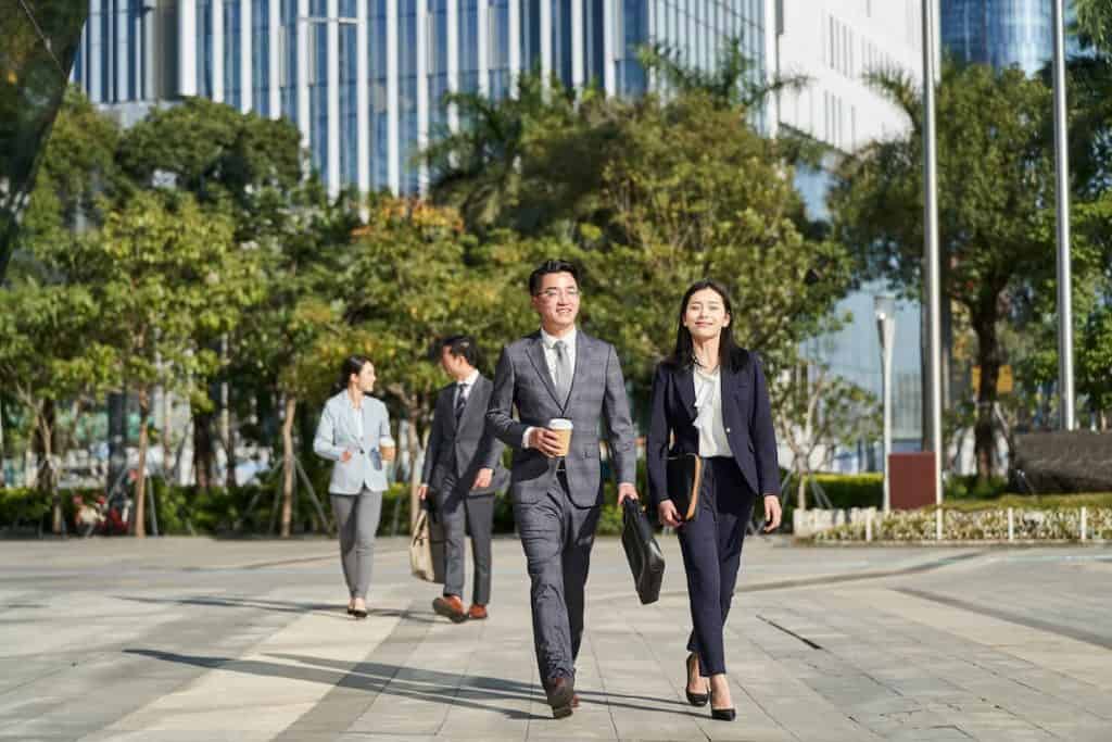 group of four young asian business people walking outdoors on street in modern city
