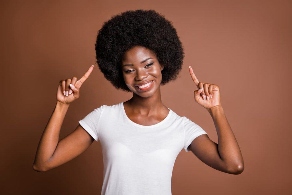 Photo portrait of girl pointing fingers on curly hair hairstyle smiling cheerful isolated on brown color background