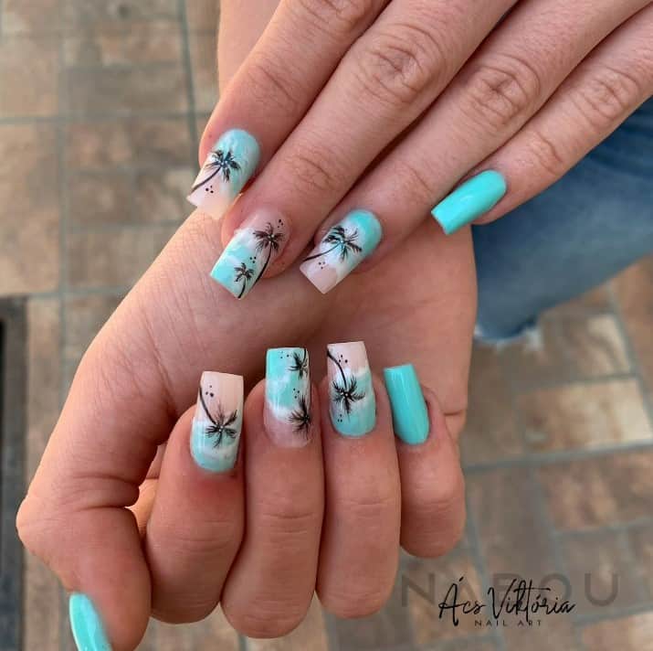 These cruise acrylic nails create a serene escape at your fingertips, with turquoise polish and intricately painted beach art featuring waves and palm tree silhouettes against the blue ocean.