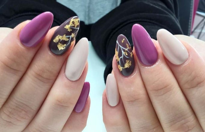 Draped in off-white, purple, and brown nails, these nails are autumn-ready, and the gold foil leaves that cascade down the branches of a few nails round off the theme.