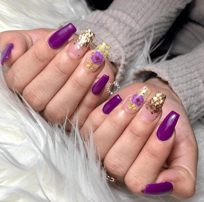 Purple reigns supreme in this acrylic purple and gold nail design, complemented by frosted clear nails that boast chunky gold glitter flakes and bright florals. 