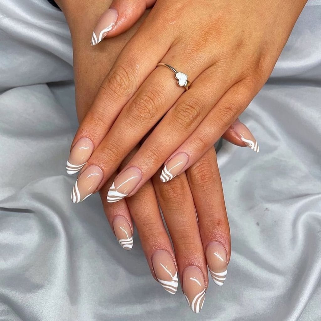 A woman's hands with traditional French manicure with these nude almond nails featuring French tips that take a creative turn by using white swirl patterns