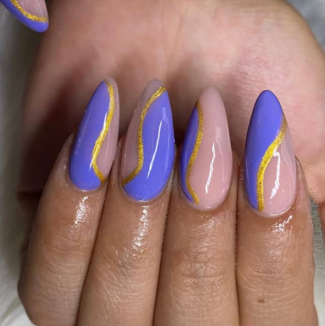 These nude almond nails in purple and gold glitter feature indigo swirls embraced by a radiant outline of sparkling gold.