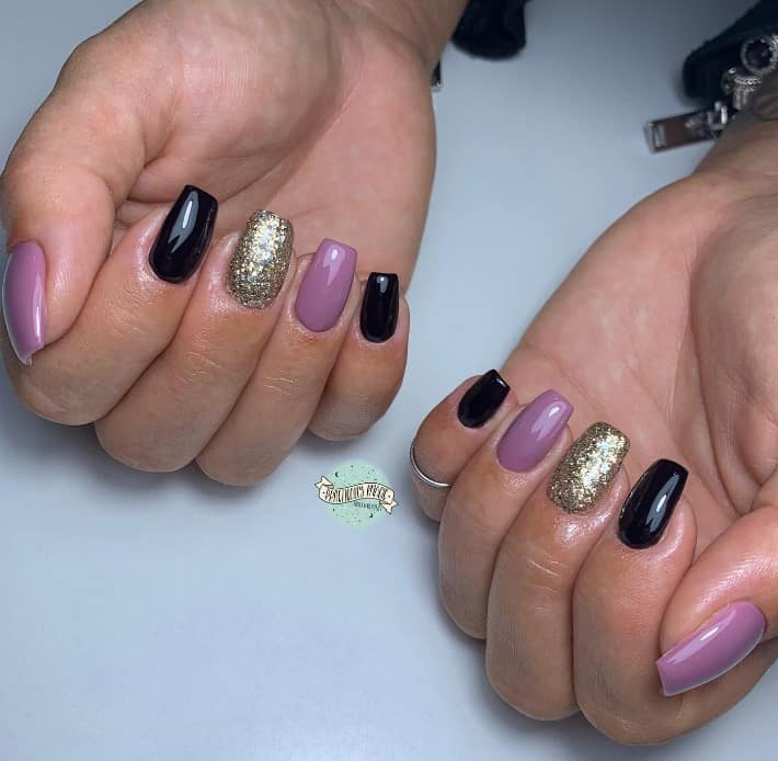 This nail design screams elegance with alternating nails in royal purple, jet black, and gold glitter. 