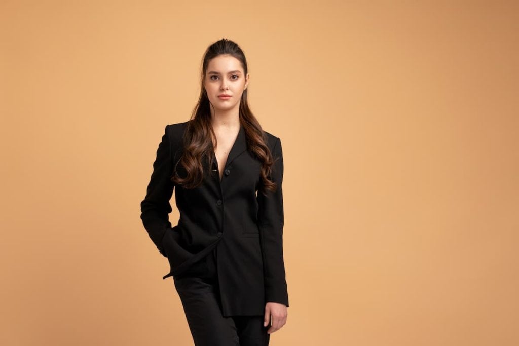 Young business woman one hand in pocket dressed black jacket standing studio isolated on color background. 