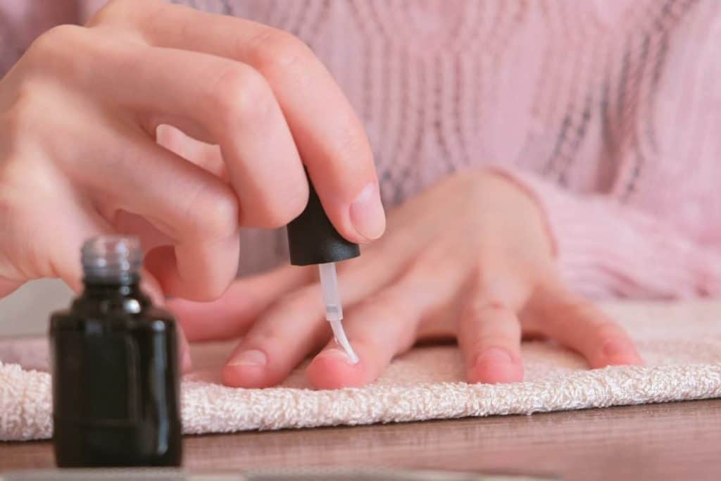 A woman applying a nail polish to her fingernails.