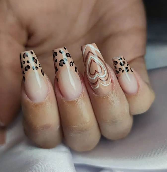 Nude nails with thick beige French tips topped with leopard spots pair with one standout brown nail layered with white and Powerpuff hearts for a touch of retro romance.