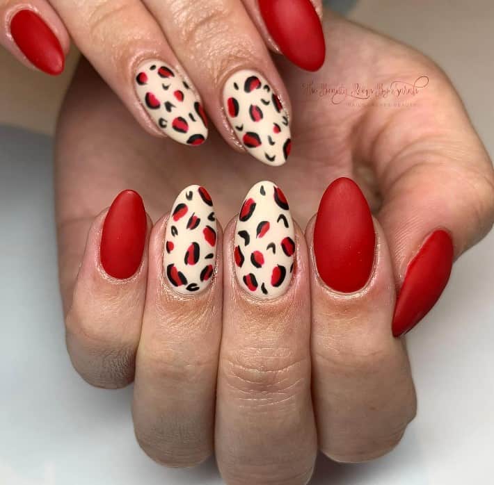 Dive into a bold statement with matte red nails! Leopard prints with red centers are artfully painted on a creamy backdrop and paired with plain red claws. 