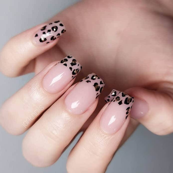 Soft glossy nude nails with delicate black leopard spots as French tips showcase a sophisticated take on the wild leopard print. 