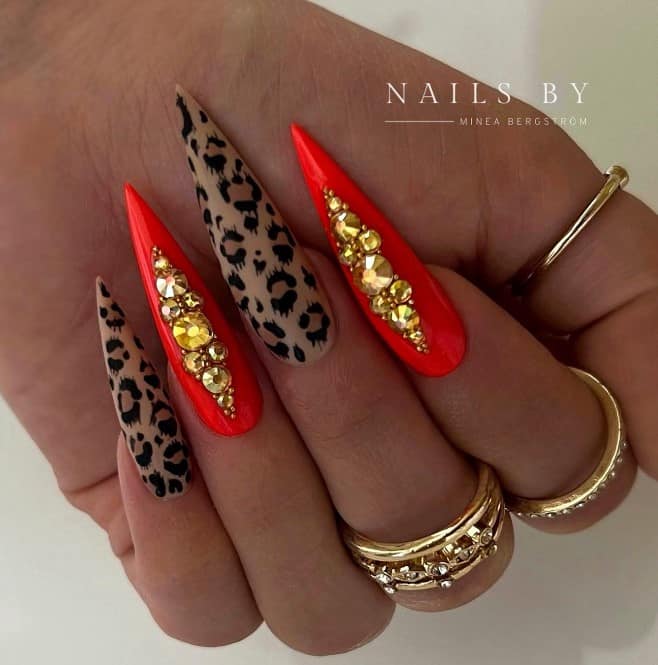 This mani showcases red-orange nails with golden rhinestones that alternate with nails decorated with leopard prints on a long brown stiletto base.