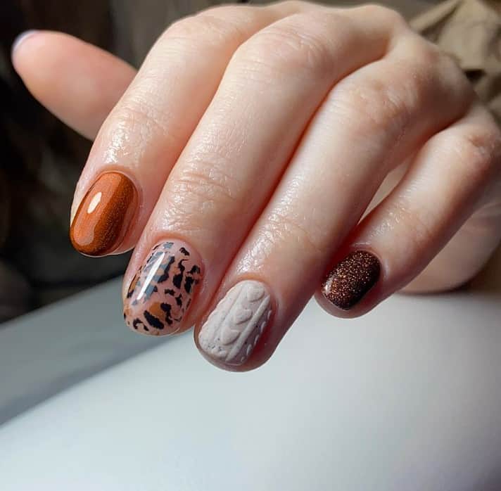 A single nail features a glossy brown leopard print on a nude backdrop. Matte nude embraces a 3D sweater pattern, while glittery burnt orange and brown nails add a sparkling contrast in this leopard nail design for short nails. 
